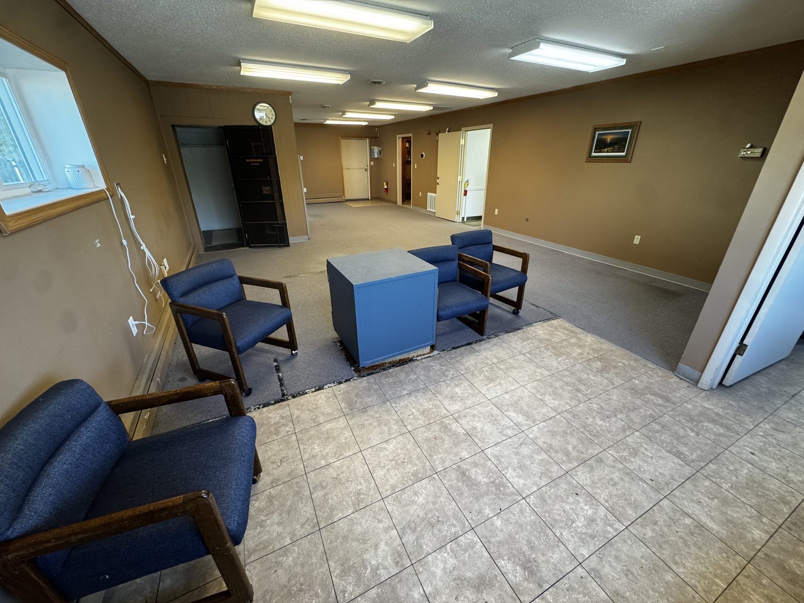 Suite A open office area with tile and carpet flooring, seating, and doorway to the former vault