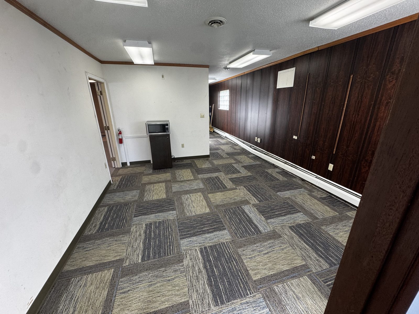 Suite B back area with carpet-tile flooring and wood-paneled wall